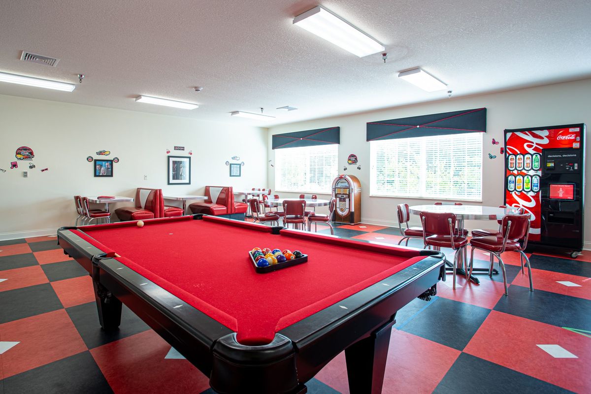 A spacious game room featuring a red-felt pool table and seating area with ample natural light.