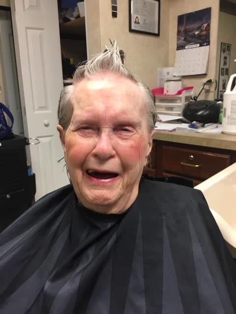 An elderly person smiling while getting a haircut in a barbershop.