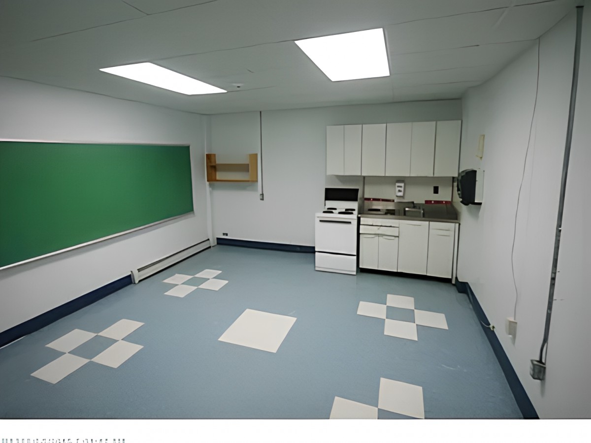 An empty classroom with a kitchenette, featuring a chalkboard and tiled flooring.
