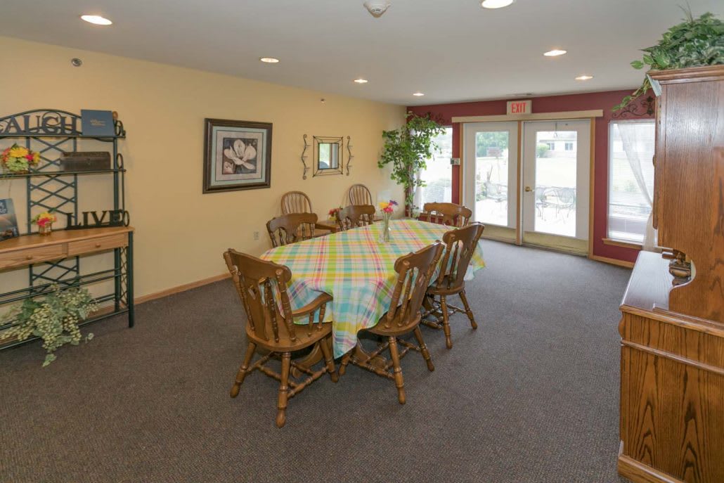 A cozy dining room with a large table and wooden chairs, featuring decorative elements and ample natural light from nearby windows.