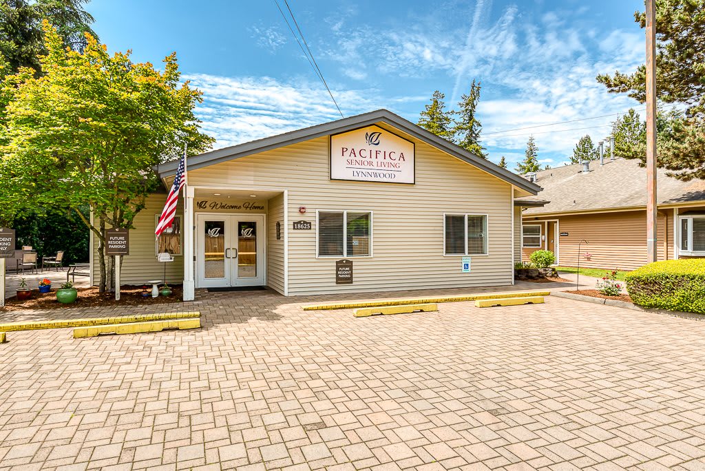 The image shows the exterior of a single-story building with an entrance and signage, surrounded by a paved parking area.