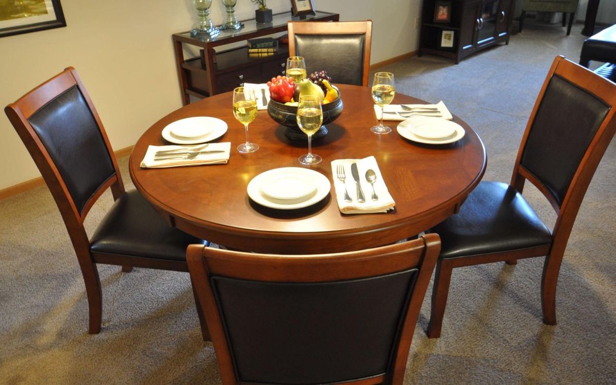 A neatly set round dining table with four place settings and a central fruit bowl.