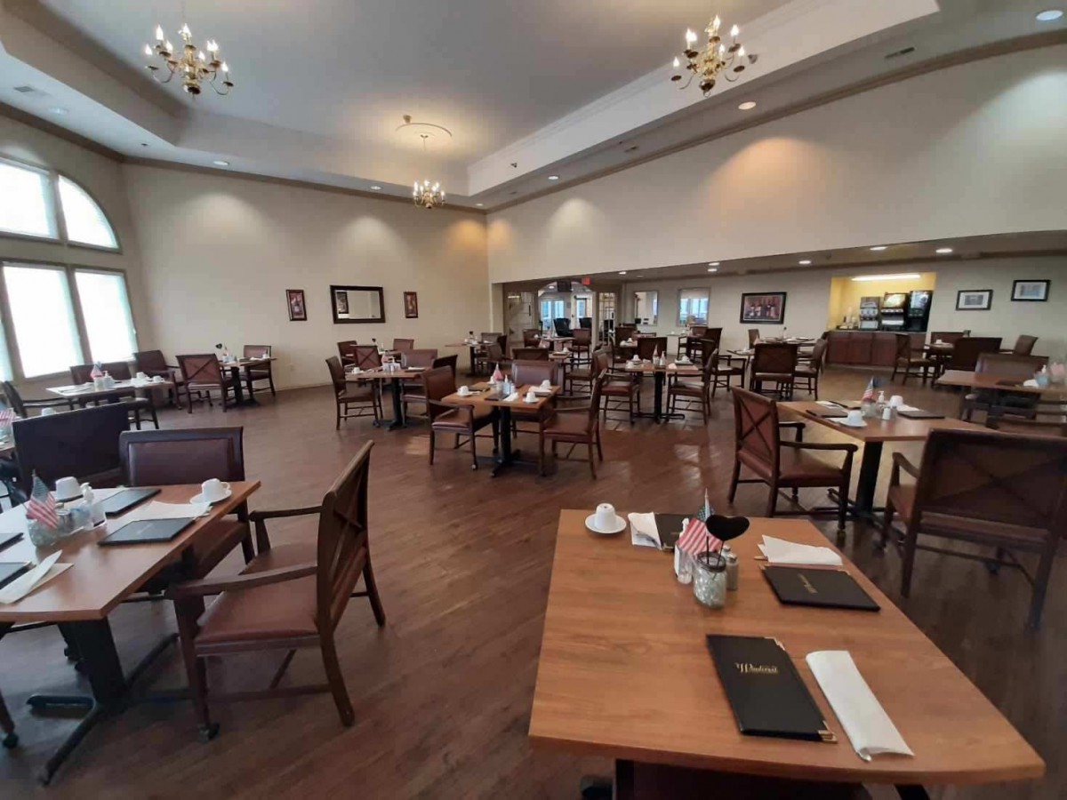 A spacious restaurant interior with neatly arranged tables and chairs, illuminated by elegant chandeliers.