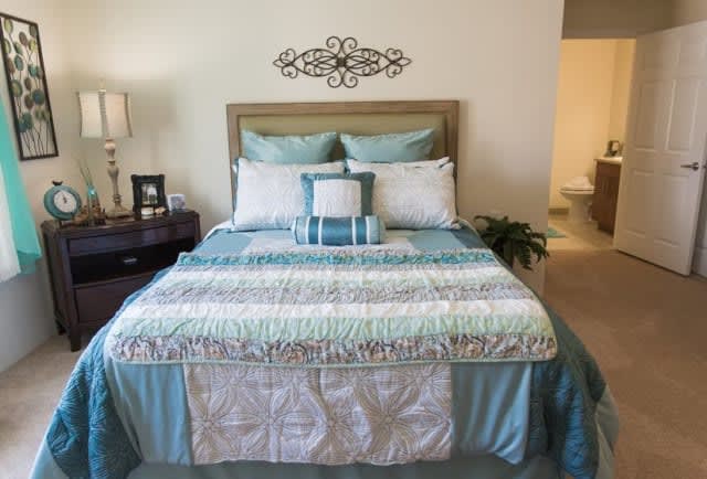 A neatly arranged bedroom featuring a bed with blue and white bedding, decorative pillows, and a bedside lamp.