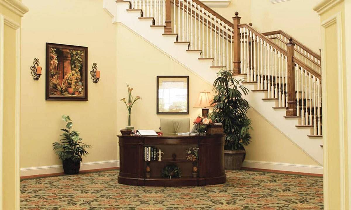 A cozy reception area with a wooden desk, carpeted floor, and staircase in the background.