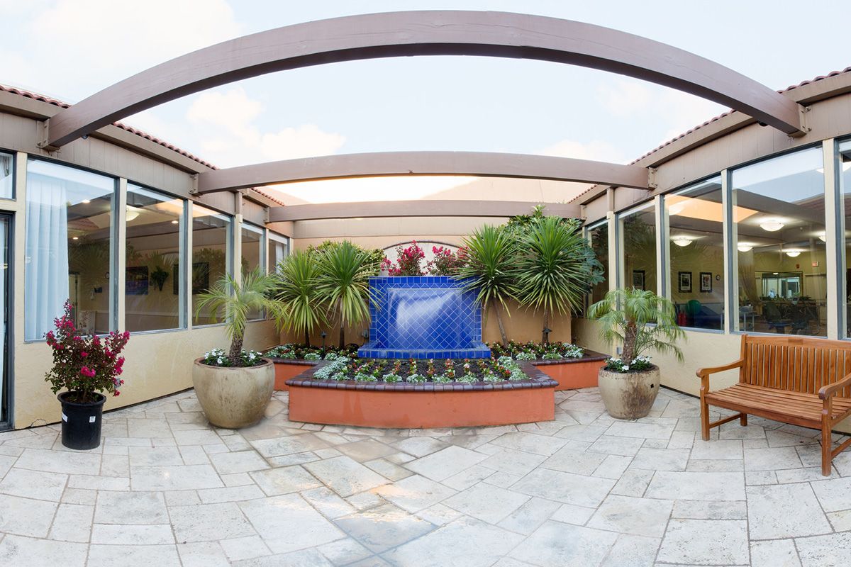A serene courtyard featuring a central fountain surrounded by potted plants and a modern roof structure.