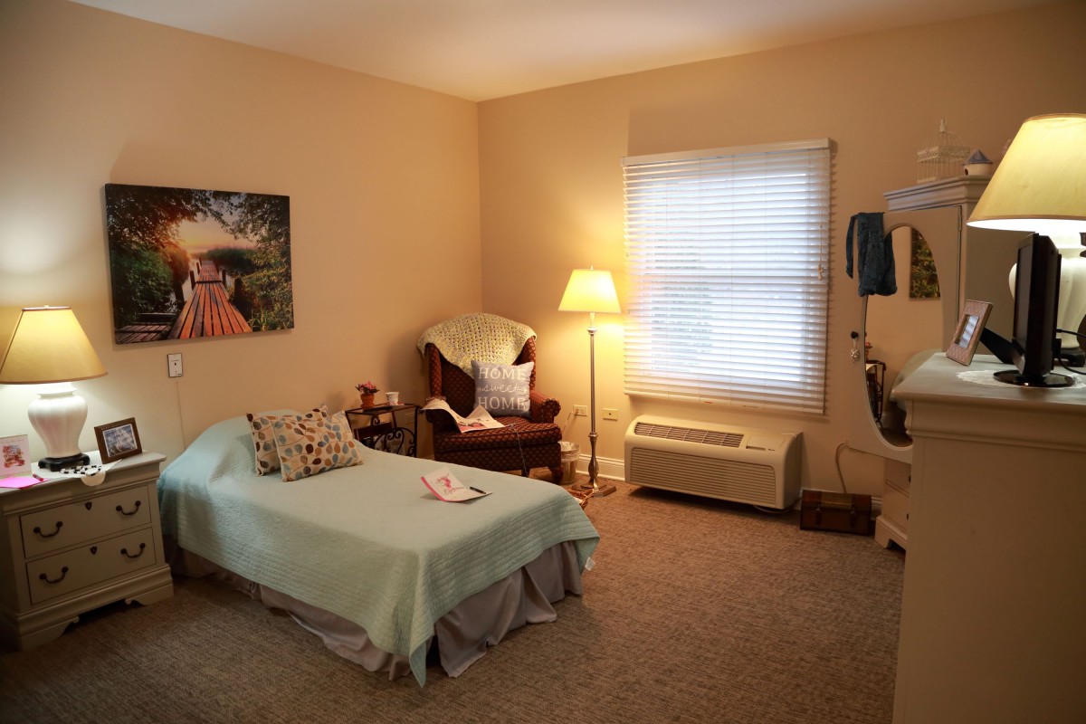 A cozy bedroom with a bed, armchair, and a standing lamp by the window.