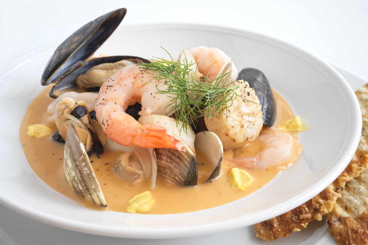 A gourmet seafood dish featuring shrimp, mussels, and clams in a creamy sauce, garnished with fresh herbs.