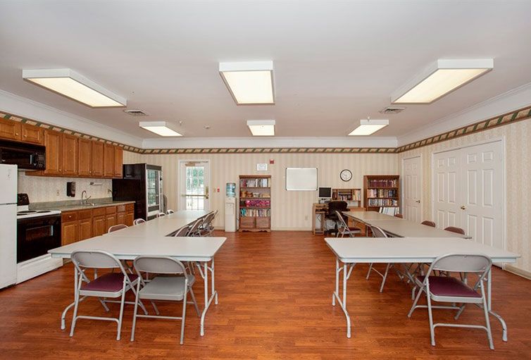 A classroom setting with tables, chairs, bookshelves, and a kitchenette area.