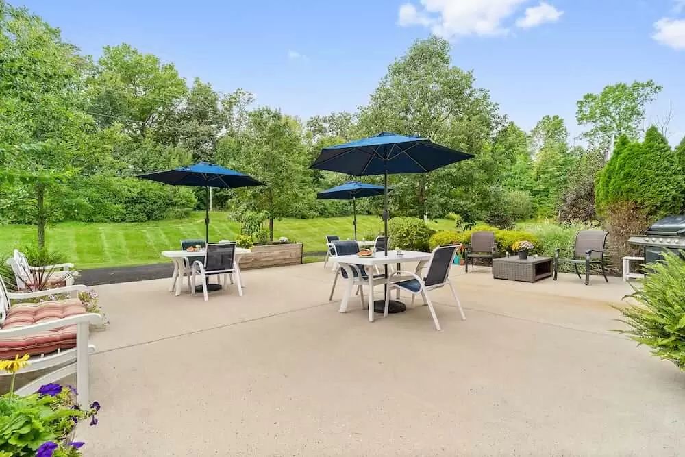 A sunny patio with tables, chairs, and umbrellas overlooking a lush garden.