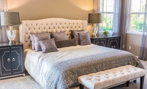 A cozy bedroom featuring a tufted headboard, decorative pillows, and a bedside lamp.