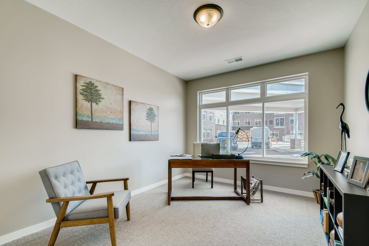 A modern office space with a wooden desk, armchair, and large window providing natural light.