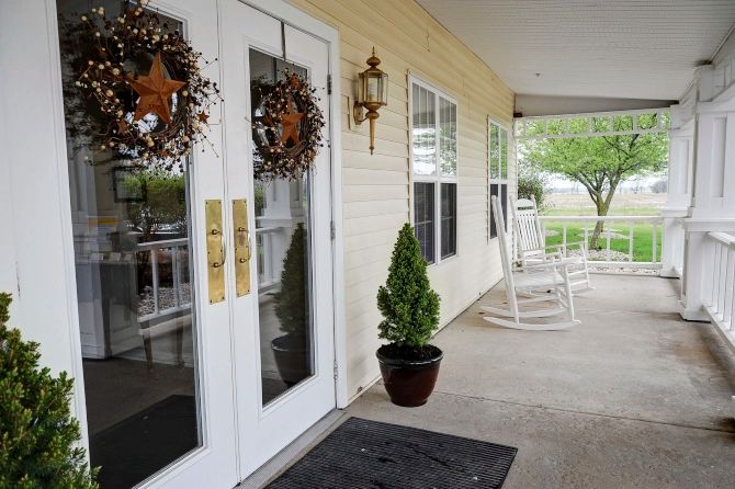 A welcoming front porch with decorative wreaths on double doors, a planter with greenery, and rocking chairs for outdoor relaxation.