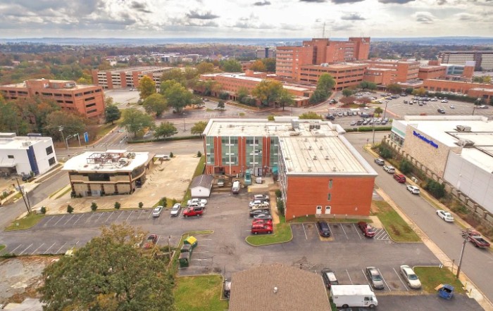 Aerial view of a cityscape featuring multiple buildings, parking areas, and a cloudy sky.