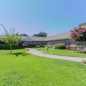 A sunny day view of a building surrounded by a lush green lawn and trees.