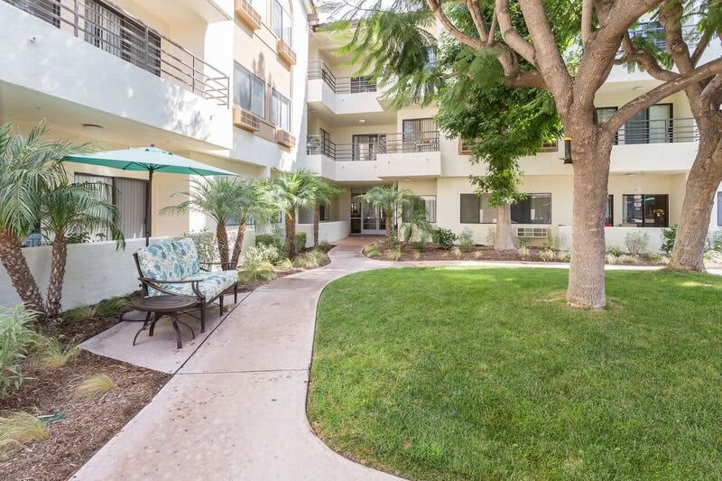 A serene courtyard of an apartment complex with lush greenery and outdoor seating.