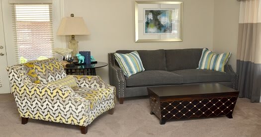 A cozy living room with a grey sofa, patterned armchair, wooden coffee table, and decorative elements.