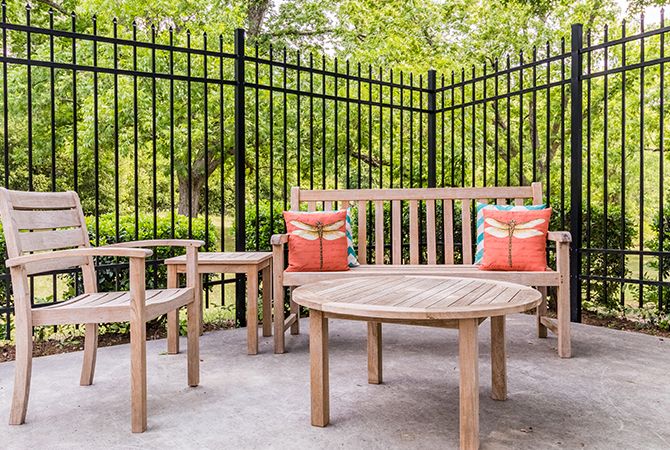 A cozy outdoor patio setup with a wooden bench, chairs, and table adorned with colorful pillows.