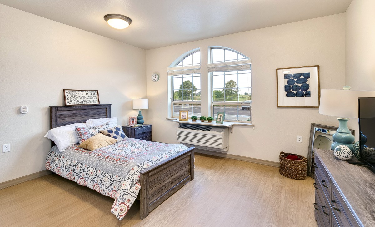 A modern and cozy bedroom with a large window offering ample natural light, featuring a neatly made bed and stylish decor.