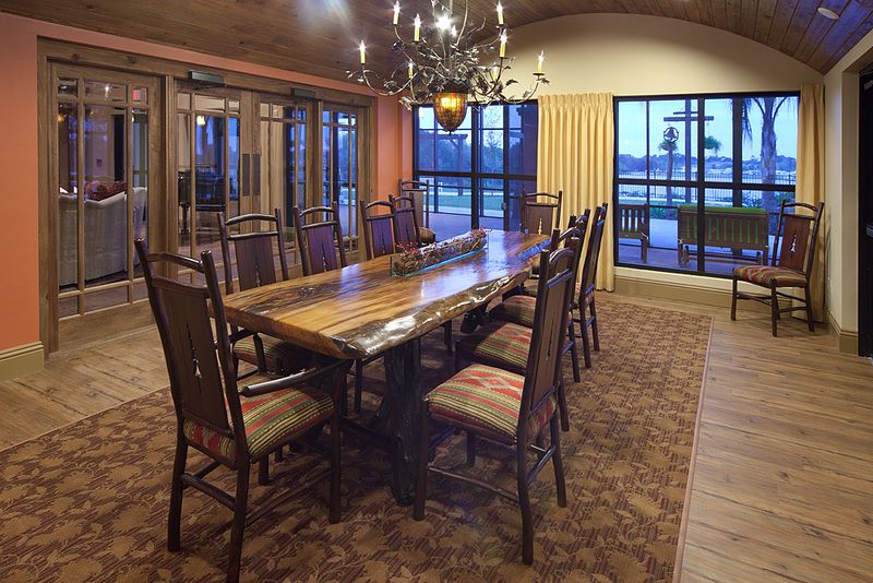 A spacious dining room with a long wooden table, surrounded by chairs, and illuminated by a chandelier.