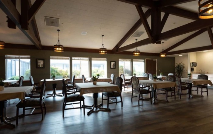 A cozy dining area with neatly arranged tables and chairs, featuring large windows and exposed wooden beams.