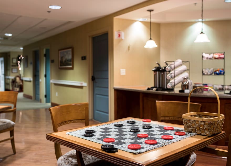 A cozy room with a checkers game set up on a table, accompanied by chairs and warm lighting.