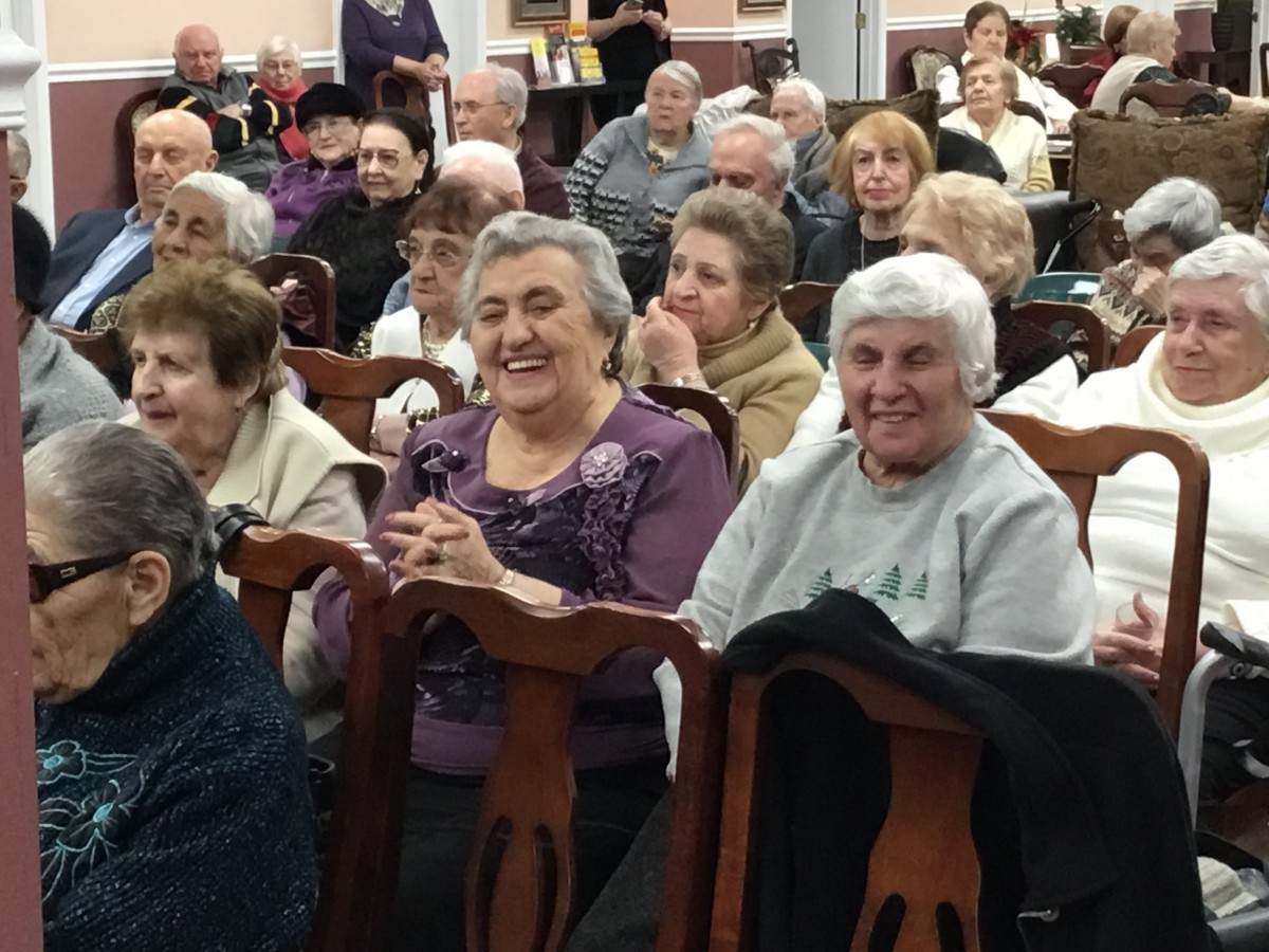 A group of elderly people smiling and gathered together indoors.