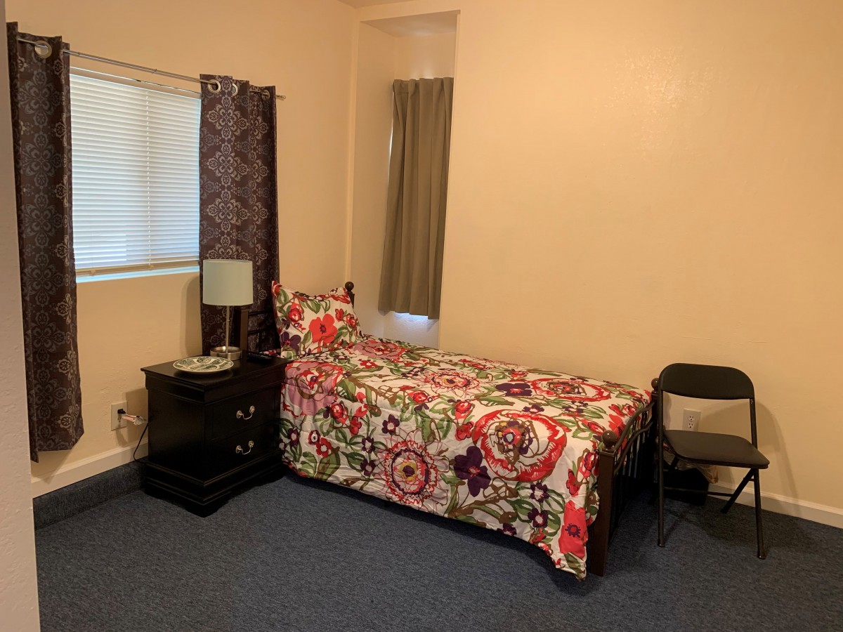 A cozy bedroom with a single bed adorned with colorful bedding, accompanied by a nightstand and lamp.