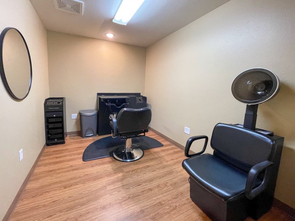 An empty hair salon with a salon chair, hair dryer, and wooden flooring.