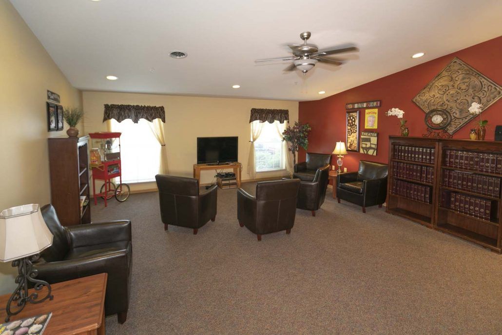 A cozy living room featuring several armchairs around a television, with a carpeted floor and warm lighting.