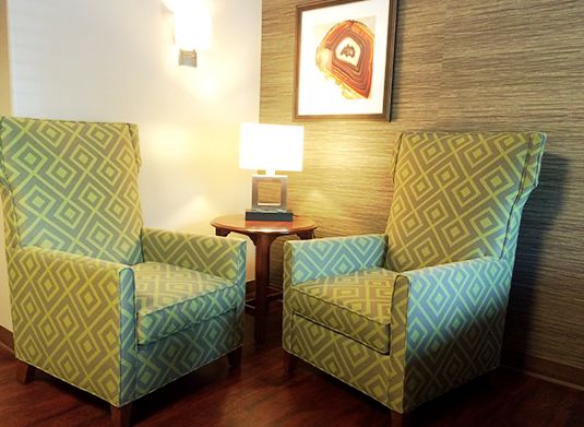 A cozy living room setup featuring two stylish armchairs, a small lamp on a wooden table, and artwork on the wall.