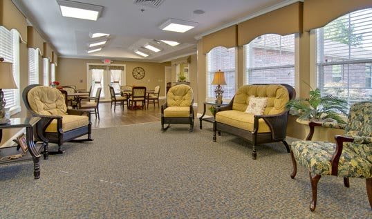 A cozy lounge area with comfortable chairs and a sofa, well-lit by large windows.