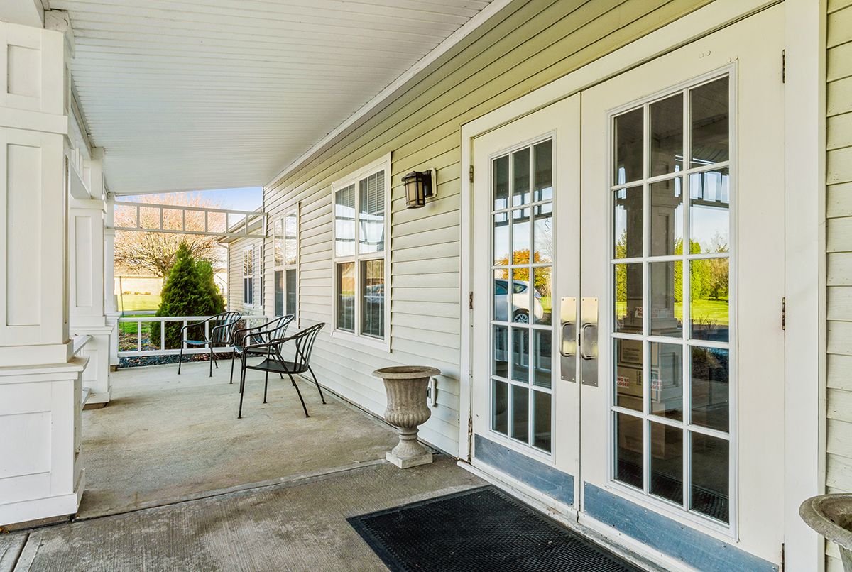 A cozy residential porch with chairs and a table next to French doors.
