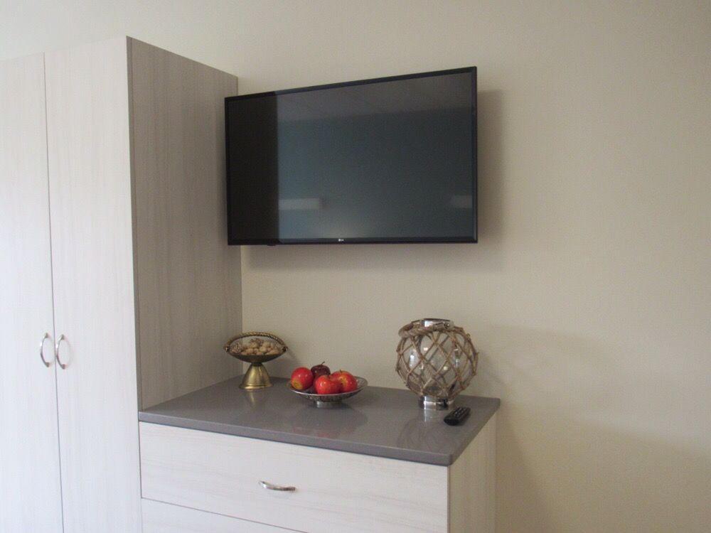 A wall-mounted television above a cabinet with decorative items including a bowl of apples and a decorative ornament.