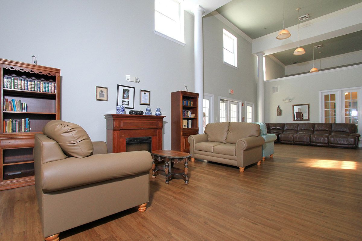 A spacious living room with sofas, a fireplace, and a bookshelf, featuring high ceilings and ample natural light from large windows.