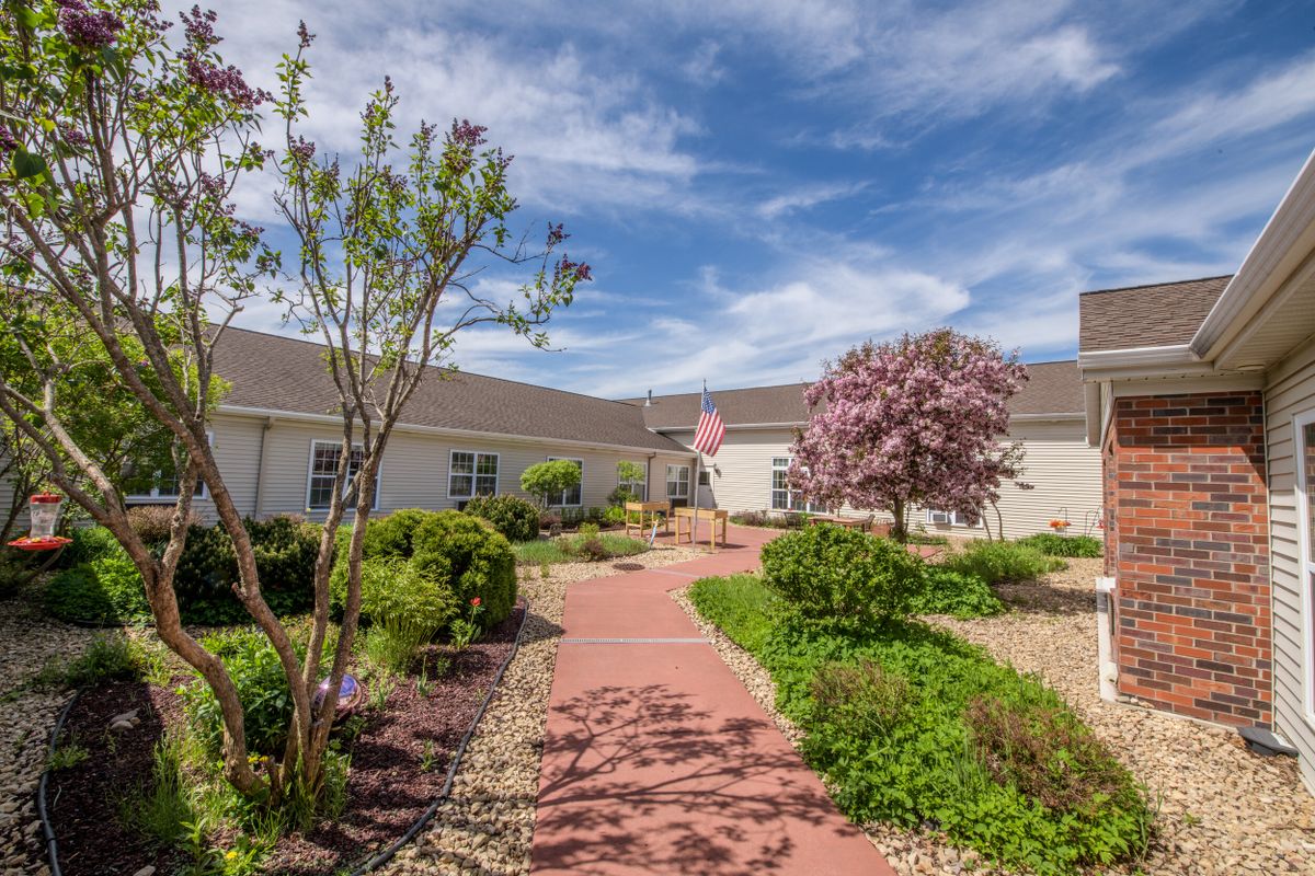 A scenic garden pathway with blooming trees and a building under a clear blue sky.