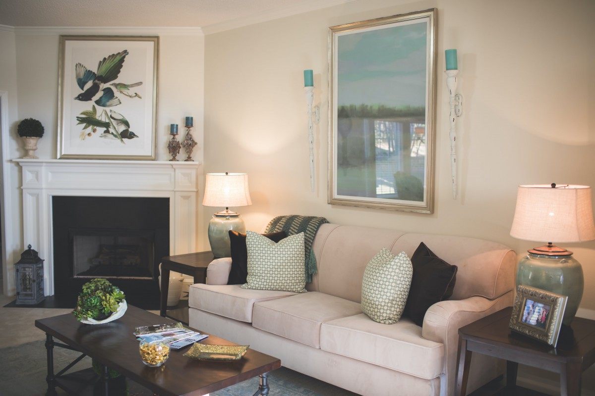 A cozy living room featuring a comfortable sofa with cushions, a coffee table, a lamp, and decorated with wall art above the fireplace.