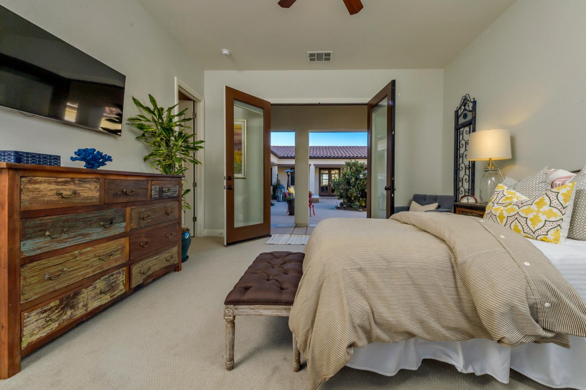 A cozy bedroom with an open door leading to a patio, featuring a bed, dresser, and decorative plant.