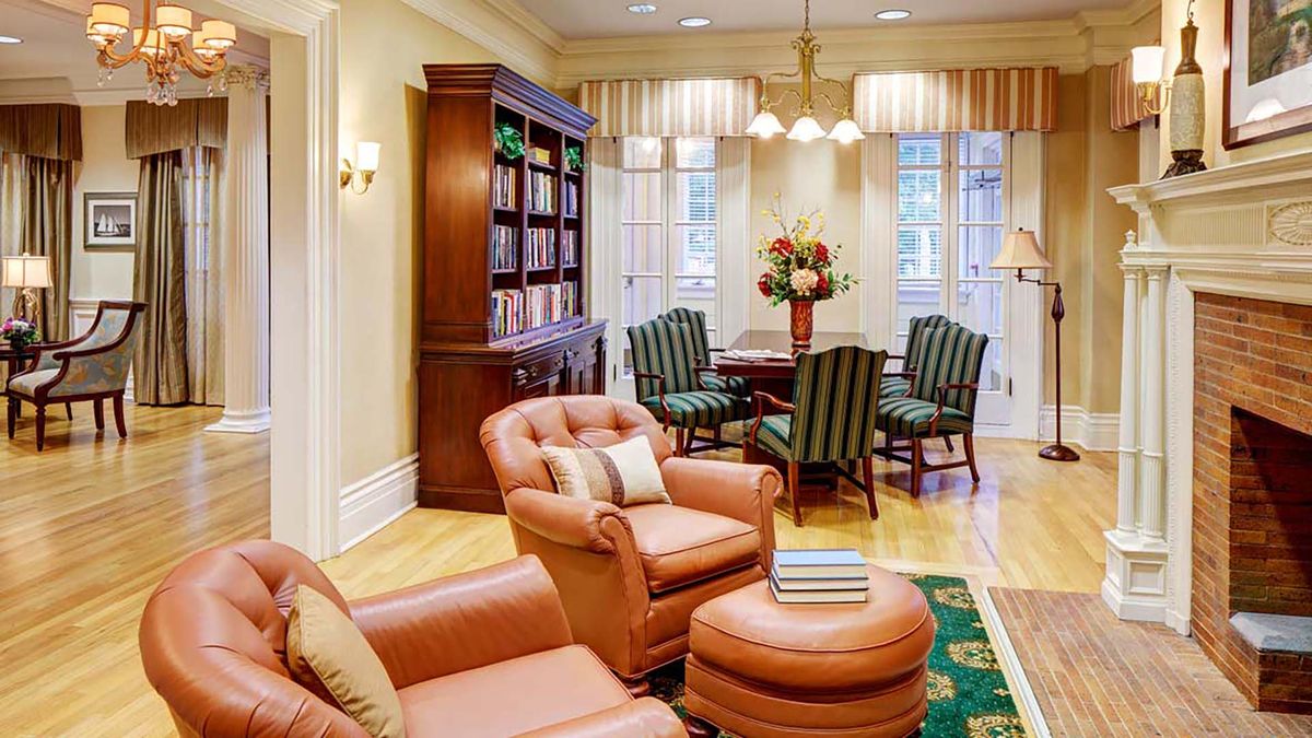 A cozy living and dining area featuring leather armchairs, a wooden bookshelf, and a dining set with striped upholstery.