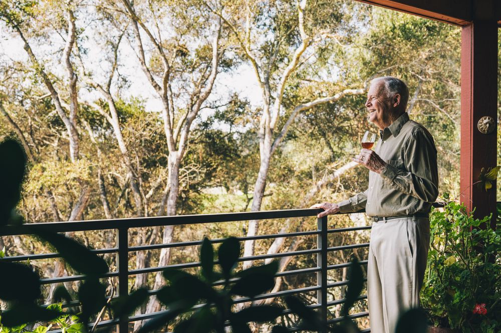 An elderly man enjoys a peaceful morning on the balcony, surrounded by trees.