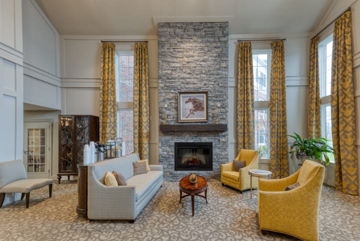 A cozy living room with a stone fireplace, elegant sofa, and two yellow armchairs.