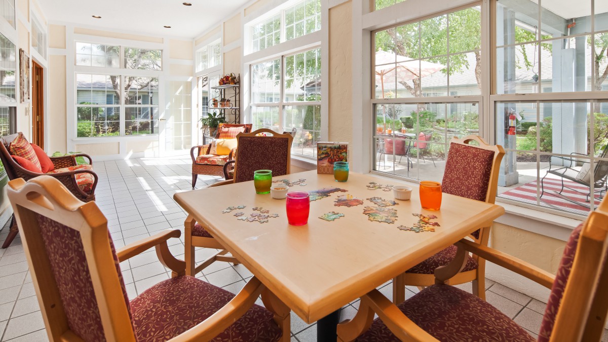A bright sunroom with a table set for refreshments, featuring colorful glasses and comfortable seating.