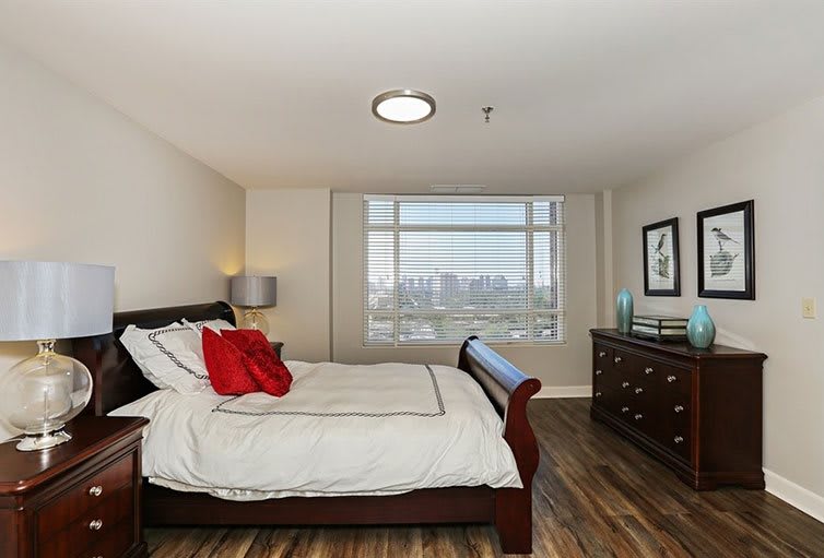 A modern bedroom with wooden flooring, a large bed, and a window overlooking a cityscape.