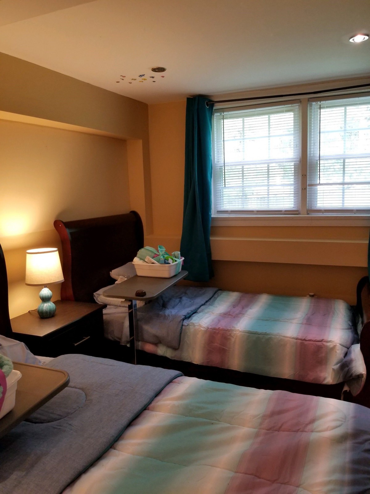 A cozy bedroom with twin beds, a lamp on the nightstand, and light streaming through the window.