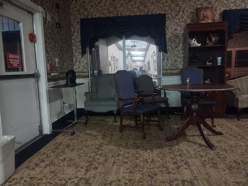 A cozy sitting area featuring a mix of chairs and a table, with warm lighting and floral wallpaper.