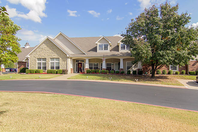 A large residential house with a porch, surrounded by a well-maintained lawn and trees under a clear blue sky.