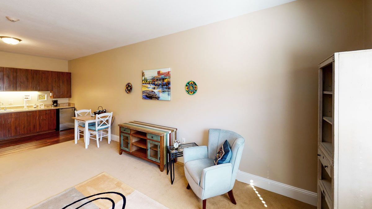 A cozy living room with an armchair, a decorative sideboard, wall art, and a dining area.