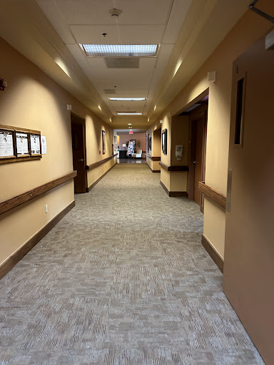 A view of a well-lit hallway with doors on either side, featuring carpeted flooring.