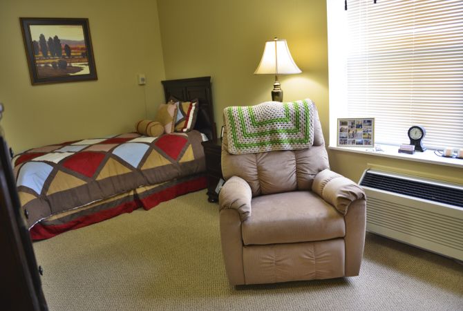 A cozy bedroom with an armchair, bed, and lamp by the window.