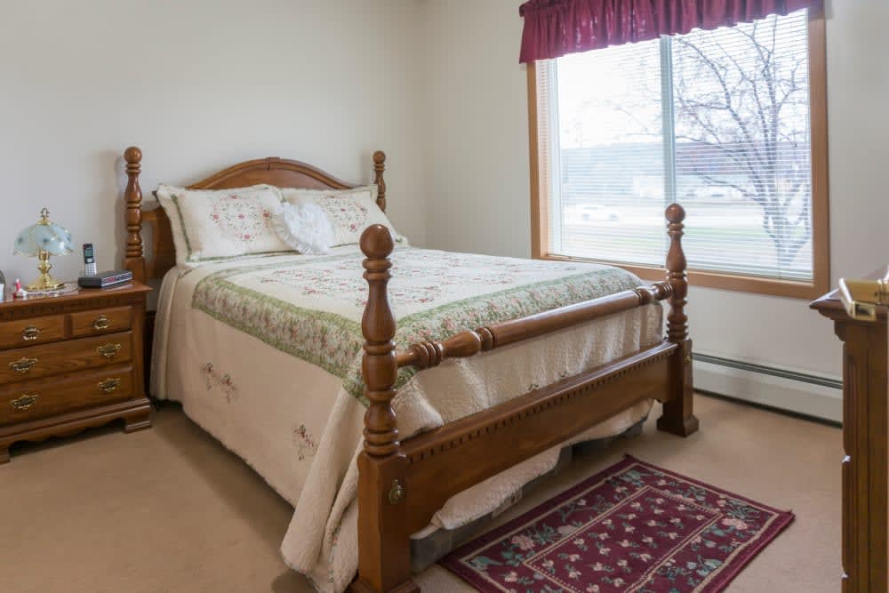 A cozy bedroom with a wooden bed and a decorative rug, featuring a large window with natural light.